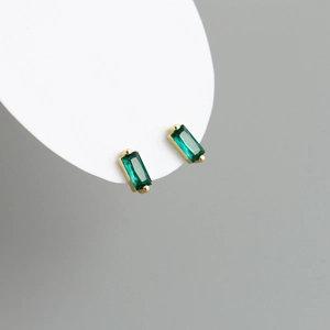 Macro detail of emerald-cut green zircon earrings with minimalist golden four-prong setting