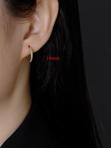 Detail van 14mm gouden oorringen met turquoise zirkonia stenen op het oor van model