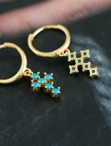 Gros plan de boucles d'oreilles croix dorées avec pavé de turquoises et fermoirs anneaux