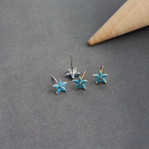 Dettaglio macro di orecchini a fiore di prugno con petali blu in montature argento e oro