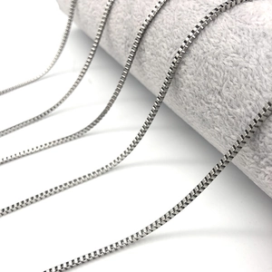 Multiple silver stainless steel box chains arranged on a plush grey texture background