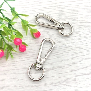 Close-up of polished silver swivel snap hooks for bags on white wood surface