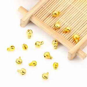 Polished gold hollow bell charms with top loops scattered on a bamboo mat background