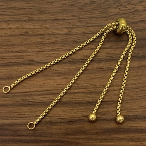 Detailopname van verstelbare gouden boxketting met schuifkraal op walnoothouten achtergrond