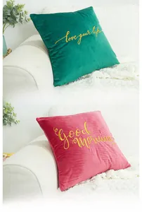 Detail of velvet pillow covers with golden embroidery and elegant lettering on a white sofa