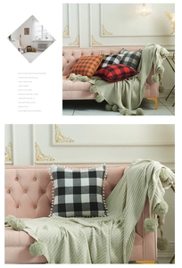 Detail of plaid cotton-linen pillowcases with white pom-pom trim on velvet sofa