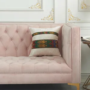 Off-white velvet pillow cover with ethnic woven ribbon patterns on a pink velvet sofa