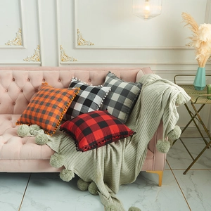 Checkered cotton-polyester pillow covers with pom-pom trim in four colors on a velvet sofa