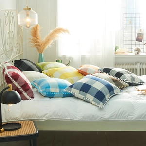 Gingham linen pillow covers with pom-poms in various colors stacked on a bed