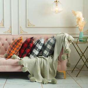 Plaid pattern cushions with pom-pom trim and a knit throw on a pink retro sofa