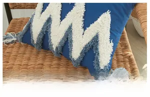 Détail de la housse de coussin bleu foncé avec franges géométriques blanches et pompons