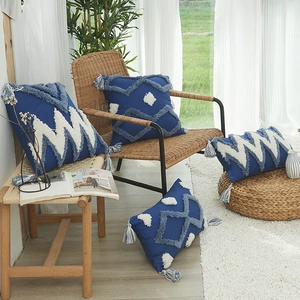 Housse de coussin géométrique bleu Klein avec broderie tuftée et pompons sur chaise rotin