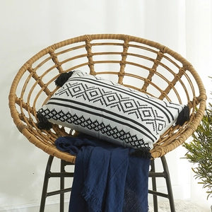 Moroccan geometric chenille throw pillow cover with black tassels on a rattan chair