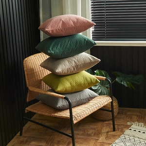 Set of minimalist embossed velvet pillow covers in five colors on a rattan chair