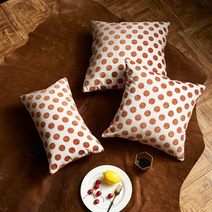 Housses de coussin texturées avec pois orange disposées sur un tapis en peau marron
