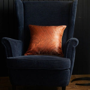 Modern jacquard throw pillow cover with bronze water ripple pattern on a blue velvet chair