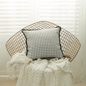 Modern black and white checkered cushion cover with fringes on a gold chair