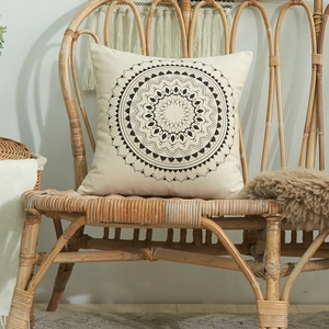 Square cotton pillow cover with black mandala pattern on a vintage rattan chair