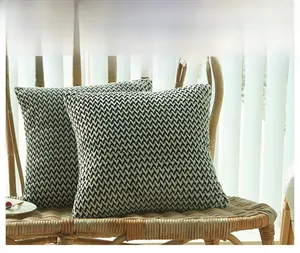 Detail shot of black and white herringbone knitted cushion covers on a rattan chair