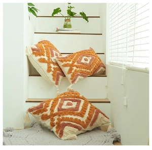 Detail of bohemian tufted pillow covers with orange geometric patterns and tassels