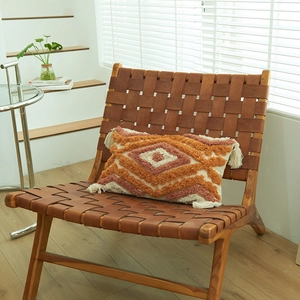 Bohemian tufted lumbar pillow with geometric diamond patterns and fringe on a leather chair