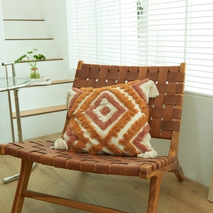Modern boho tufted geometric throw pillow with tassels on a leather chair