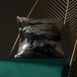 Cuscino decorativo nero moderno con motivi astratti oro e argento su una poltrona di lusso