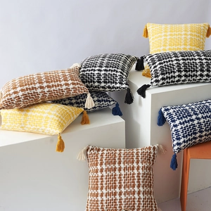 Nordic checkered knit throw pillows with tassels displayed on geometric white stands