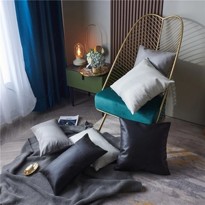 Minimalist textured throw pillows in grey, white, and brown on a velvet chair and floor
