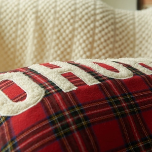 Red plaid Christmas pillow cover with white fuzzy embroidery on a cozy knit blanket