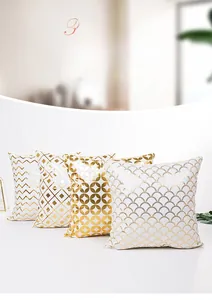 Detail of four white pillow covers with gold geometric patterns like diamonds and waves