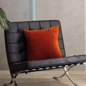 Bright orange velvet square throw pillow with unique pleated texture on a black leather chair