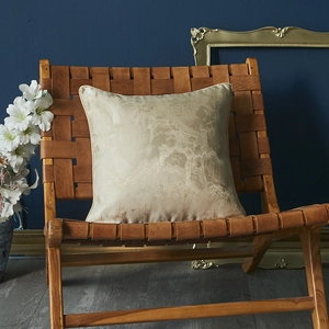 Champagne satin cushion cover with marble pattern on a brown leather woven chair