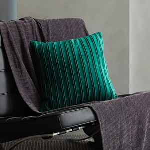 Modern velvet striped pleated throw pillow in emerald green on luxury black leather chair
