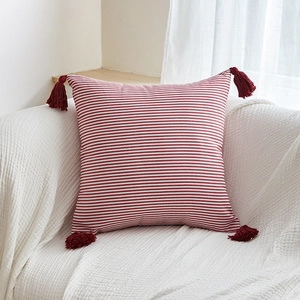 Square red and white striped throw pillow with burgundy fringe on a white sofa
