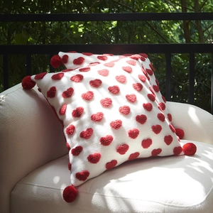 Weißes Kissen mit roten 3D-Herzen und Pompons auf einem modernen Gartensofa