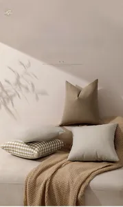 Close-up of textured checked and striped cushion covers on a beige sofa with warm shadows