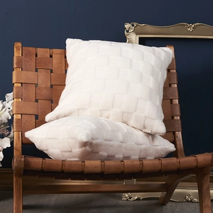 Set of two white checkered plush pillows on a stylish leather chair in a home setting