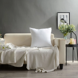 Close-up of a white leaf-embroidered plush pillow case on a cozy beige fabric sofa