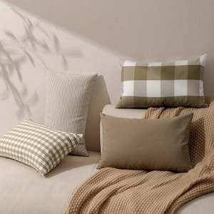 Set of four khaki and beige checkered and striped decorative cushion covers in warm sunlight