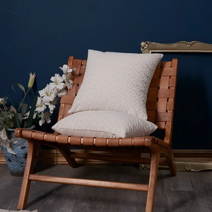 Pair of cream chenille throw pillows with 3D leaf texture on a brown leather chair