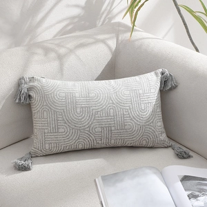 Light gray geometric jacquard pillow with elegant tassels on a cozy beige sofa