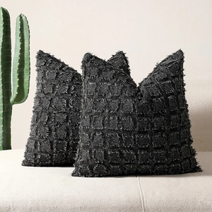 Set of two black tufted checkered pillow covers on a white sofa with 3D fringe texture