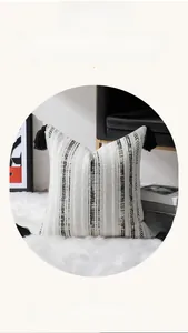 Détail d'une housse de coussin jacquard en chenille avec pompons sur un tapis en peluche