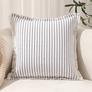 Modern blue striped throw pillow with fringe trim on a cream sofa in home setting