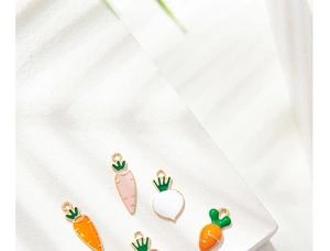 Close-up of colorful enamel carrot charms on a white display with green leaves