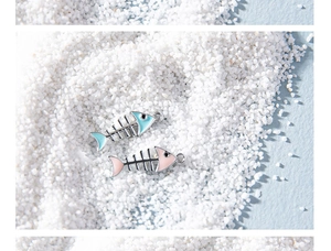 Macro view of blue and pink fishbone alloy pendants on a beach sand background