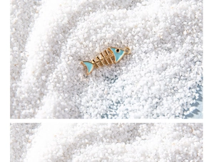 Detailed close-up of a blue enamel fishbone pendant on a decorative white sand base