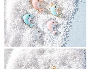 Macro view of colorful enamel dolphin pendants for DIY jewelry on white sand background