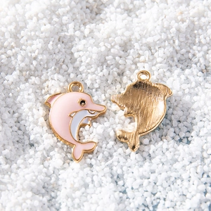 Pink and white enamel dolphin pendants with golden metal edges on a sandy white background